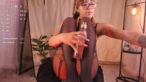 Media: Video of a woman in a black lingerie set, sitting on a chair, holding a glass bottle, with a large mirror and plants in the background.