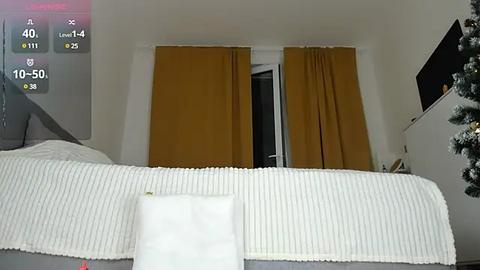 Media: Video of a cozy bedroom with a white bed, mustard-yellow curtains, and a small TV on a shelf, taken from a first-person perspective.