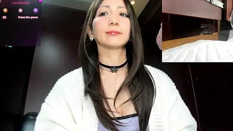 Media: Video of a young Asian woman with long, straight black hair, wearing a white knitted cardigan over a light purple top. She has a small, delicate necklace and subtle makeup. Background shows a dark room with a wooden bed frame.