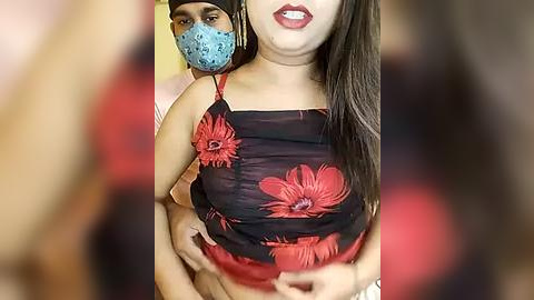 Media: Video of a woman with medium skin tone, wearing a black floral dress with red flowers, and a blue surgical mask. She has long dark hair and red lipstick.