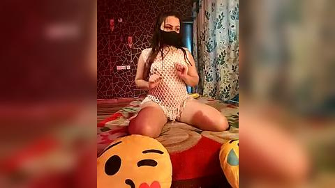 Media: Video of a woman in a white fishnet bodysuit, black face mask, and knee-high socks, sitting on a bed with cartoon pillows, in a dimly lit, patterned room.