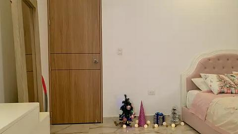 Media: Video of a minimalist, modern bedroom with a wooden wardrobe, pastel pink bed, and festive decorations including a Christmas tree, ornaments, and tinsel.