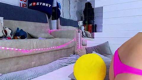 Media: Video of a brightly lit room with a modern sofa, bright pink wall, and a yellow balloon.