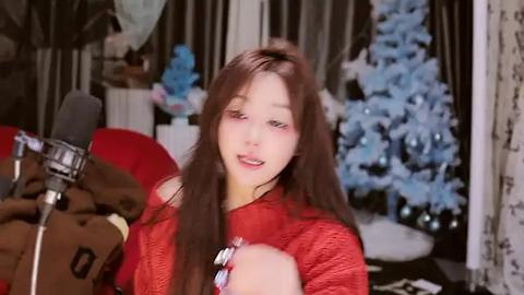 Media: Video of a young Asian woman with long brown hair, wearing a red sweater, singing into a microphone, surrounded by festive decorations including a Christmas tree and snowflakes.