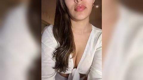 Media: Video of a young woman with long, dark hair, wearing a low-cut, white crop top, partially covering her breasts, puckering her lips in a pout.