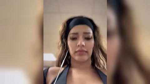 Media: Video of a young woman with light brown skin, long wavy hair, and a black headband, wearing headphones, appearing to be in a meditative or focused state.