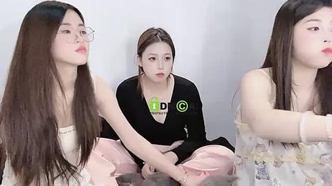 Media: Video of two young East Asian women with long black hair, one in a pink dress, the other in a black top, sitting on a bed, looking sad.