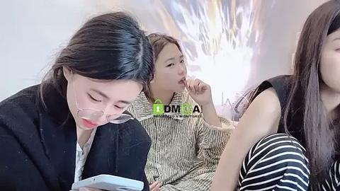 Media: Video of three young Asian women, one reading, one eating, one texting, in a modern, brightly lit room with abstract art on the wall.