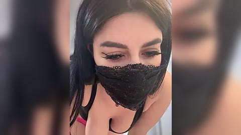 Media: Video of a young woman with long, straight black hair, wearing a black lace mask over her mouth, and a black spaghetti strap top, blurred background.