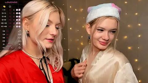 Media: Video of two young women with fair skin, one blonde and the other with blonde hair in a hat, smiling in a cozy room with string lights.