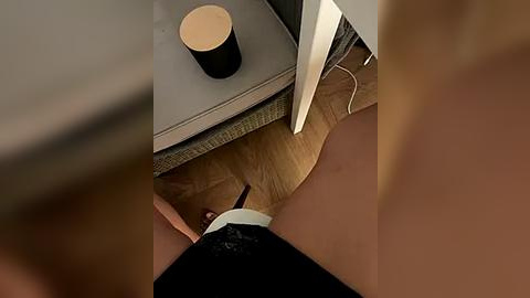 Media: Video of a person's bare legs on a wooden floor, with a black cup and white charger cord visible on a gray table. The scene suggests a casual, indoor setting.