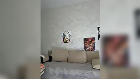 Media: Video of a minimalist living room with a beige sofa adorned with colorful art prints, including a pop art Marilyn Monroe portrait. The walls are light gray, creating a serene atmosphere.