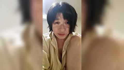 Media: A blurred video of a distressed, short-haired Asian woman in a beige robe, her face marked with tears, standing in a dimly lit room.