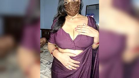 Media: Video of a middle-aged woman with a medium complexion, wearing a purple saree and face mask, standing in a dimly lit bedroom with a bed visible in the background.