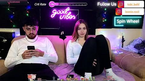 Media: Video of a young man and woman in a cozy living room, watching TV. Neon lights and colorful decor adorn the background.