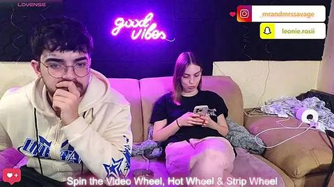 Media: Video of a young man and woman watching YouTube on a couch, neon \"good vibes\" sign in background.