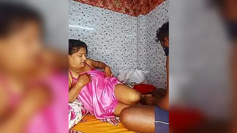 Media: Video of an Indian woman in a pink sari, lying on a bed in a tiled room, receiving medical attention from a man in a blue shirt.