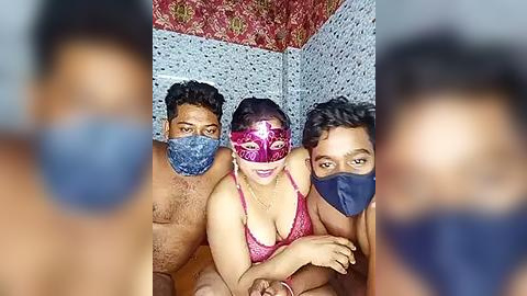 Media: Video of three South Asian adults, two men and a woman, wearing face masks. The woman, in a pink lace bra, has medium breasts and light skin. Background features tiled walls and a floral patterned ceiling.