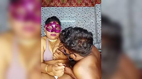 Media: A video of a topless man kissing a woman in a purple mask, both wearing ornate jewelry, set against a colorful, patterned backdrop.