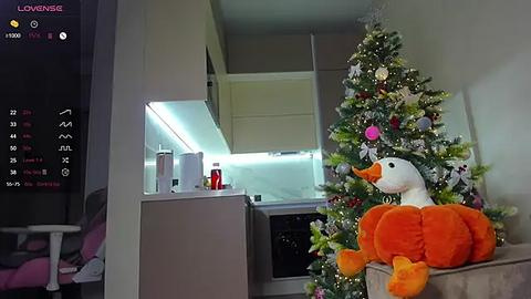 Media: A video of a cozy living room with a decorated Christmas tree featuring a plush duck ornament, alongside a modern kitchen with white cabinets and a glowing blue LED strip.