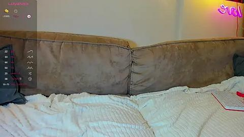 Media: Video of a messy bed with a beige suede headboard, white and red sheets, a black pillow, and a partially visible red object on the right side.