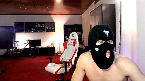 Media: Video of a bare-chested man in a black balaclava and white sneakers, seated in a red and white gaming chair, with a red carpeted room in the background.