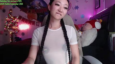 Media: Video of an Asian woman with long braids in a sheer white top, standing in a festive, cozy bedroom with holiday decorations, including a Christmas tree and stuffed animals.