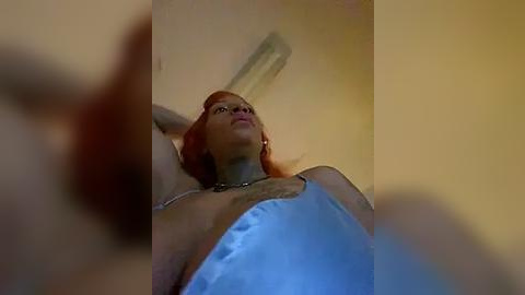 Media: A video shows a woman with short, red hair, wearing a blue tank top, looking upwards, possibly in a bathroom with beige walls and a white light fixture.