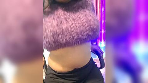 Media: Video of a woman with fair skin wearing a purple fuzzy crop top and black pants, standing in a blurred, colorful background.