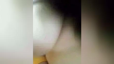 Media: A blurry, low-resolution video depicts a person's upper body in a dimly lit room. The subject appears to be leaning against a wall, with indistinct features due to the poor image quality. The background is indistinguishable, but the lighting suggests an indoor setting.