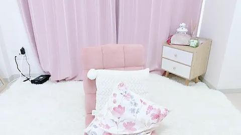 Media: A video of a pastel-themed baby room with pink curtains, a soft pink armchair, a white crib with a floral blanket, a wooden nightstand, and a plush bunny toy.