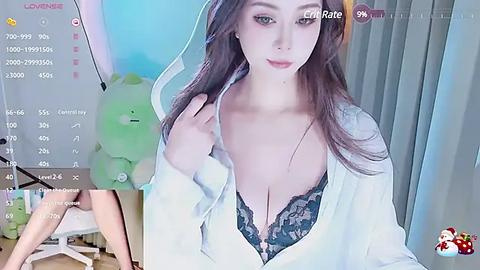 Media: Video of an East Asian woman with long brown hair, wearing a white robe exposing a green lace bra. Background includes a green bear plush toy and a TV screen with a \"Live\" overlay.