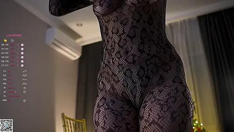 Media: A video of a woman in a black lace bodysuit, showing her curvaceous figure and ample breasts. The background features a modern room with dark curtains, a gold chair, and an air conditioner.