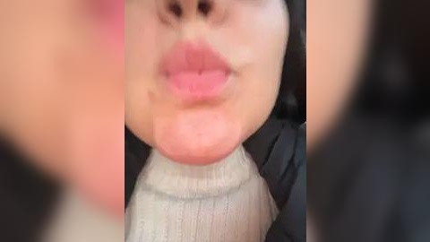 Media: Video of a close-up of a young girl with light skin, pursed lips, and a light grey sweater, blurred background.