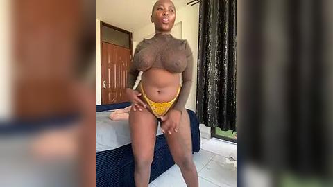 Media: A video of a confident, dark-skinned woman with large breasts and a curvy physique, wearing a sheer, brown top and yellow panties, standing in a modern bedroom with a bed and curtains.