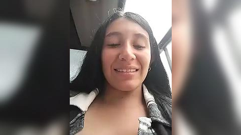 Media: Video of a young Hispanic woman with long black hair, wearing a black jacket, smiling with closed eyes in a car.