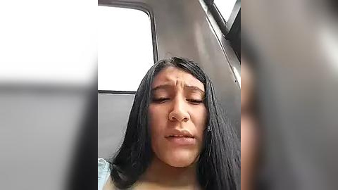 Media: Video of a young Asian woman with long black hair, wearing a white shirt, seated in a car with a neutral expression.