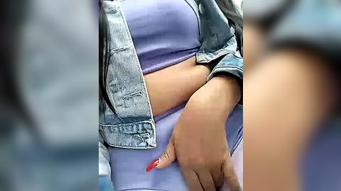 Media: Video of a person with a light brown complexion, wearing a light blue top and denim jacket, with a hand with red nail polish on the waist, creating a casual, everyday style.