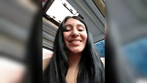 Media: Video of a smiling Asian woman with long black hair, wearing a black top, sitting in a car with tinted windows.