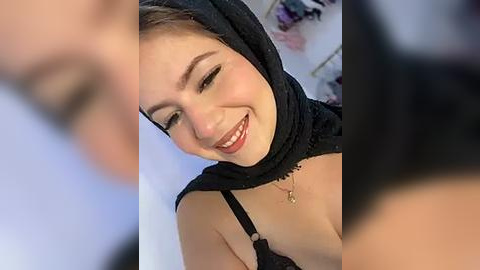 Media: A video of a smiling, light-skinned woman with short brown hair, wearing a black hijab and a black lace bra, set against a blurred, softly lit background.