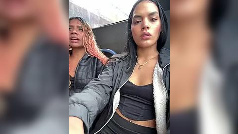 Media: Video of two women in casual attire, one with pink braids and a black jacket, the other with long black hair and a black jacket, sitting in a car.