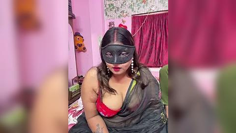 Media: Video of a plus-sized woman with light skin, wearing a black mask, red bra, and black sari, sitting on a bed with pink walls, red curtains, and stuffed toys.