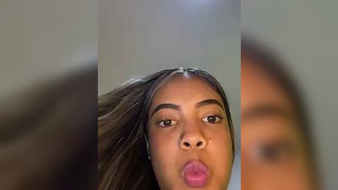 Media: Video of a young Black woman with medium brown skin, wearing a nose ring, and making a pouty face, with blurred background.