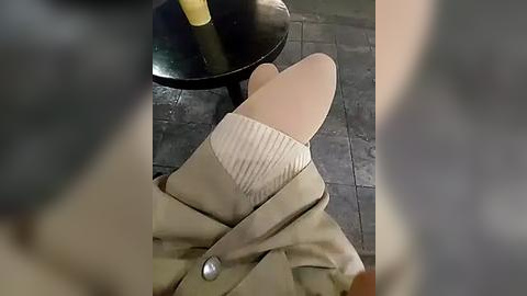 Media: Video of a person's feet in tan slippers, partially covered by a beige coat, on a tiled floor. A yellow mop handle is visible in the background.