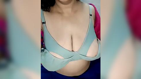 Media: Video of a woman with medium skin tone, wearing a light blue bra with visible cleavage, over a red and blue top. Her dark hair is partially visible.