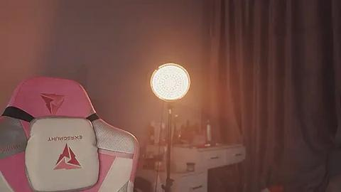 Media: Video of a pink and white gaming chair with \"Xtrfy\" logo, illuminated by a bright, circular lamp; dimly lit room with a desk, scattered items, and dark curtains in the background.