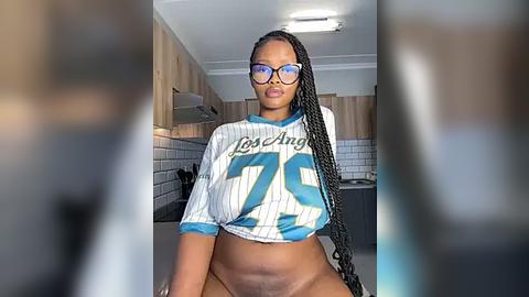 Media: Video of a Black woman with braided hair, wearing glasses, a Los Angeles Angels jersey, and no pants, in a modern kitchen.