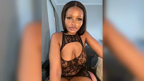 Media: Video of a Black woman with medium brown skin and shoulder-length straight hair, wearing a black lace bodysuit with a cutout revealing her cleavage. She is seated in a chair, indoors, with a blurred background.