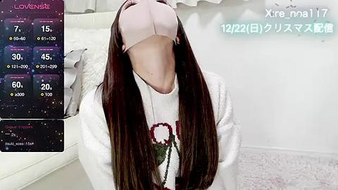 Media: Video of a person wearing a white headband, pink face mask, and white sweater with a reindeer pattern, kneeling on a white carpet in a minimalist, light-colored room.