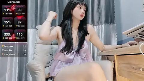 Media: A video of an East Asian woman with long black hair in a light purple, see-through lace camisole, sitting at a desk in a modern, well-lit room.